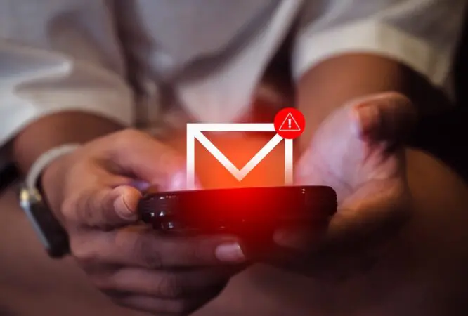 SMS spam and fake text message phishing from scammer concept. System hacked warning alert, email hack, scam malware spreading virus on message alert virtual on mobile phone screen in woman's hands.